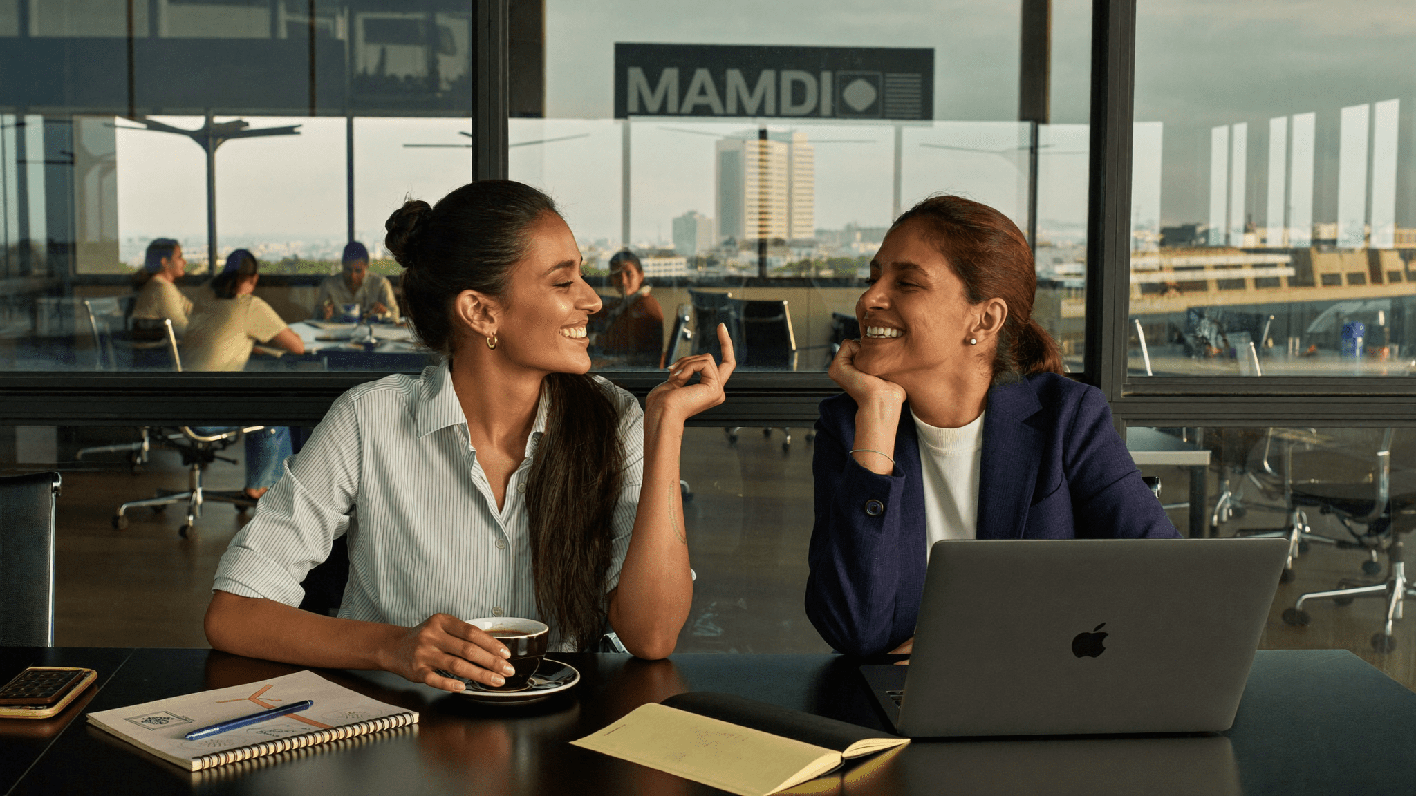 Two Indian women professionals discuss DPDP audit over coffee in glass conference room