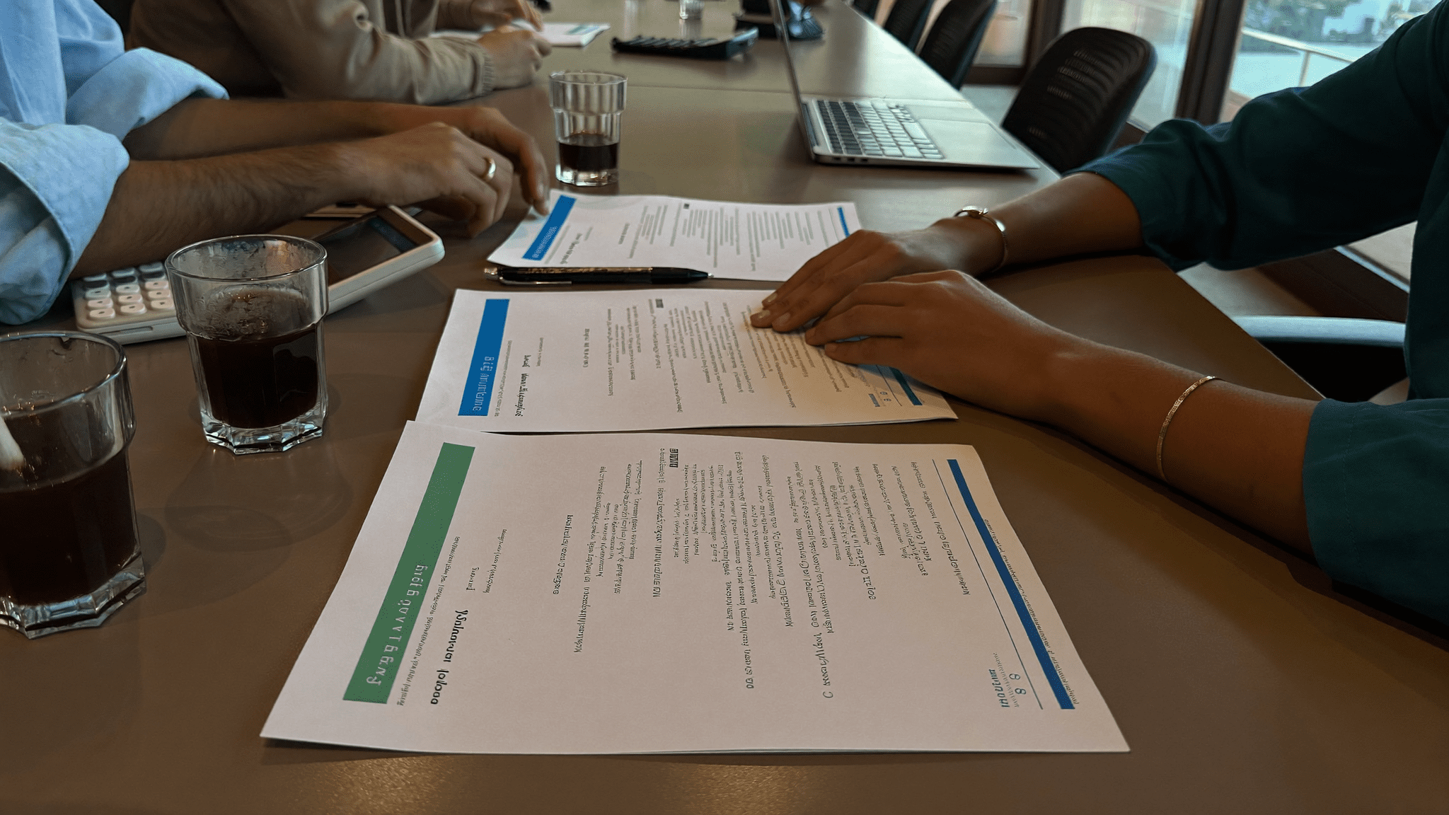 Hands of Mumbai BKC fintech IT lead and CFO over a meeting table with three printed MDM quote sheets each with a different colored band