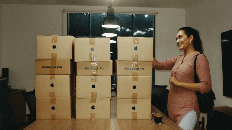 Hardware practice lead beside 42 stacked MacBook boxes on a Bengaluru creative agency boardroom table on a rainy Saturday morning