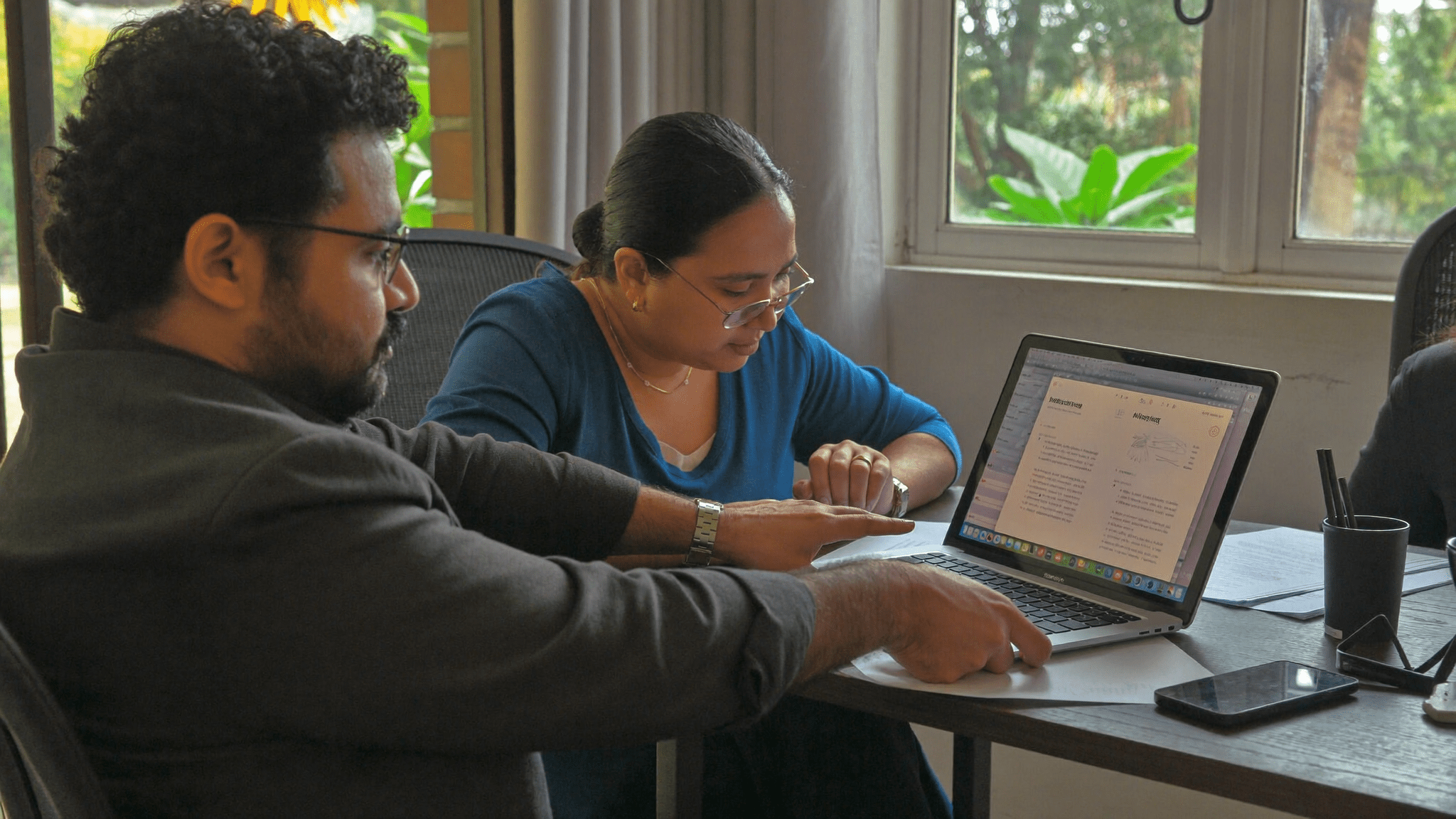 Indian Finance head turns laptop spreadsheet to show HR head across table both leaning in