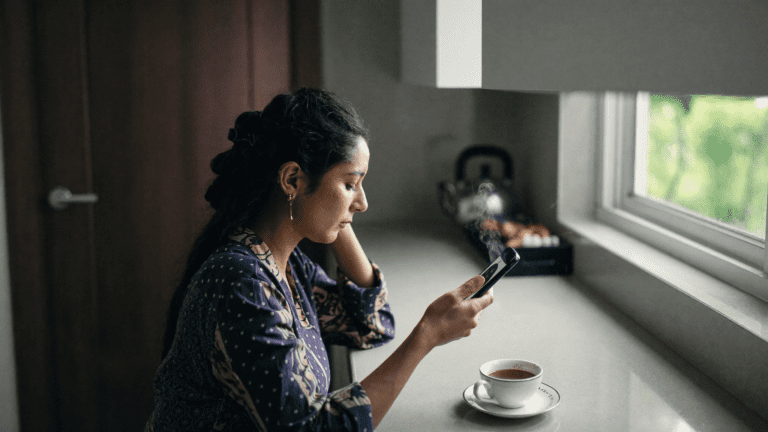 Indian IT manager candid moment in Mumbai kitchen looking at her phone in morning light