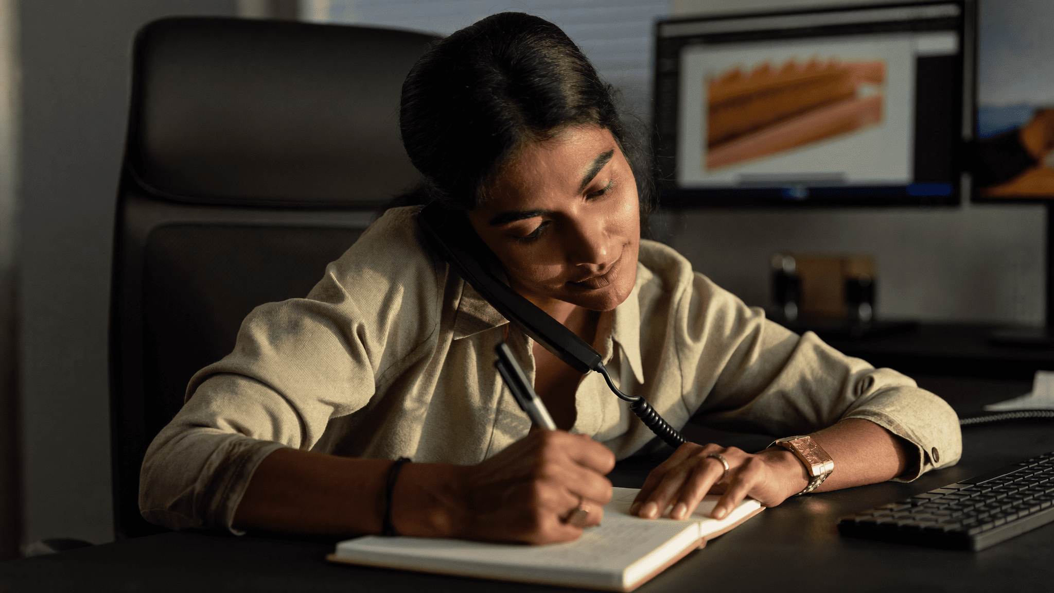 Indian IT manager in focused flow state on phone call writing notes at her desk