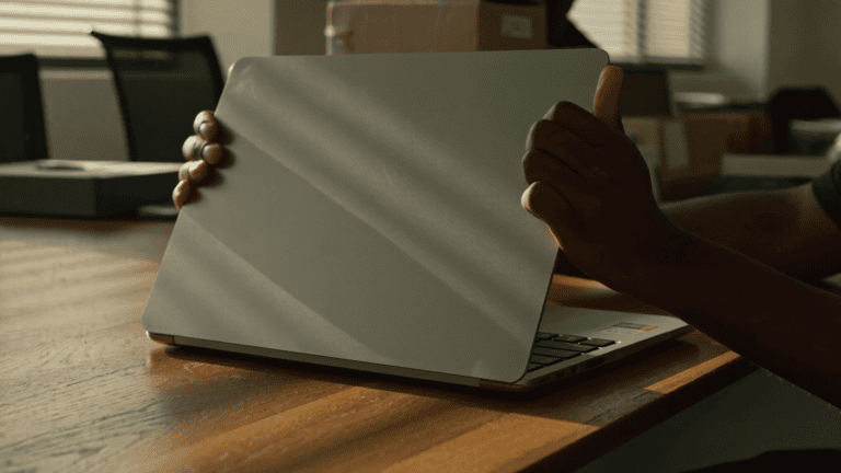 An IT operations manager lifting the lid of a new company Mac on a bare desk on the first morning of an Apple device rollout