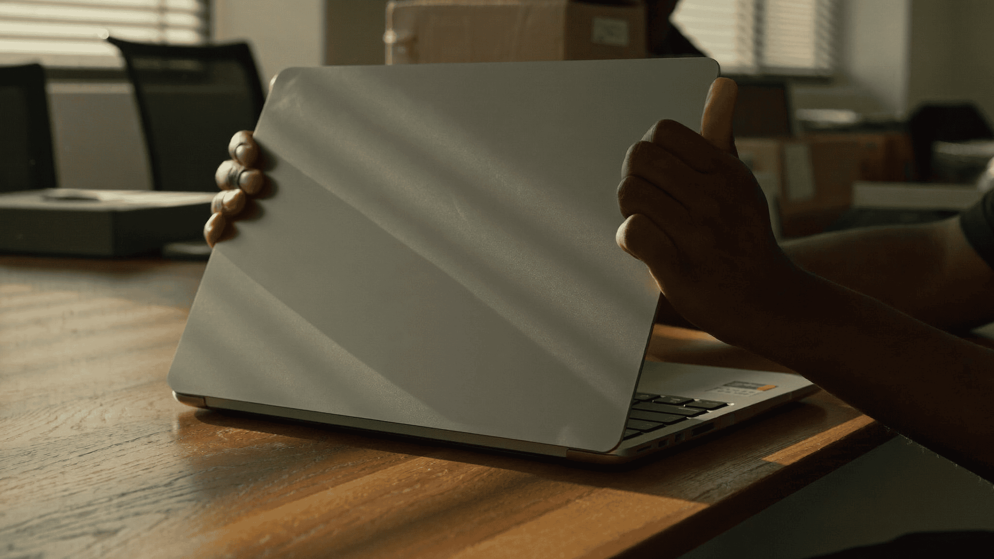 An IT operations manager lifting the lid of a new company Mac on a bare desk on the first morning of an Apple device rollout