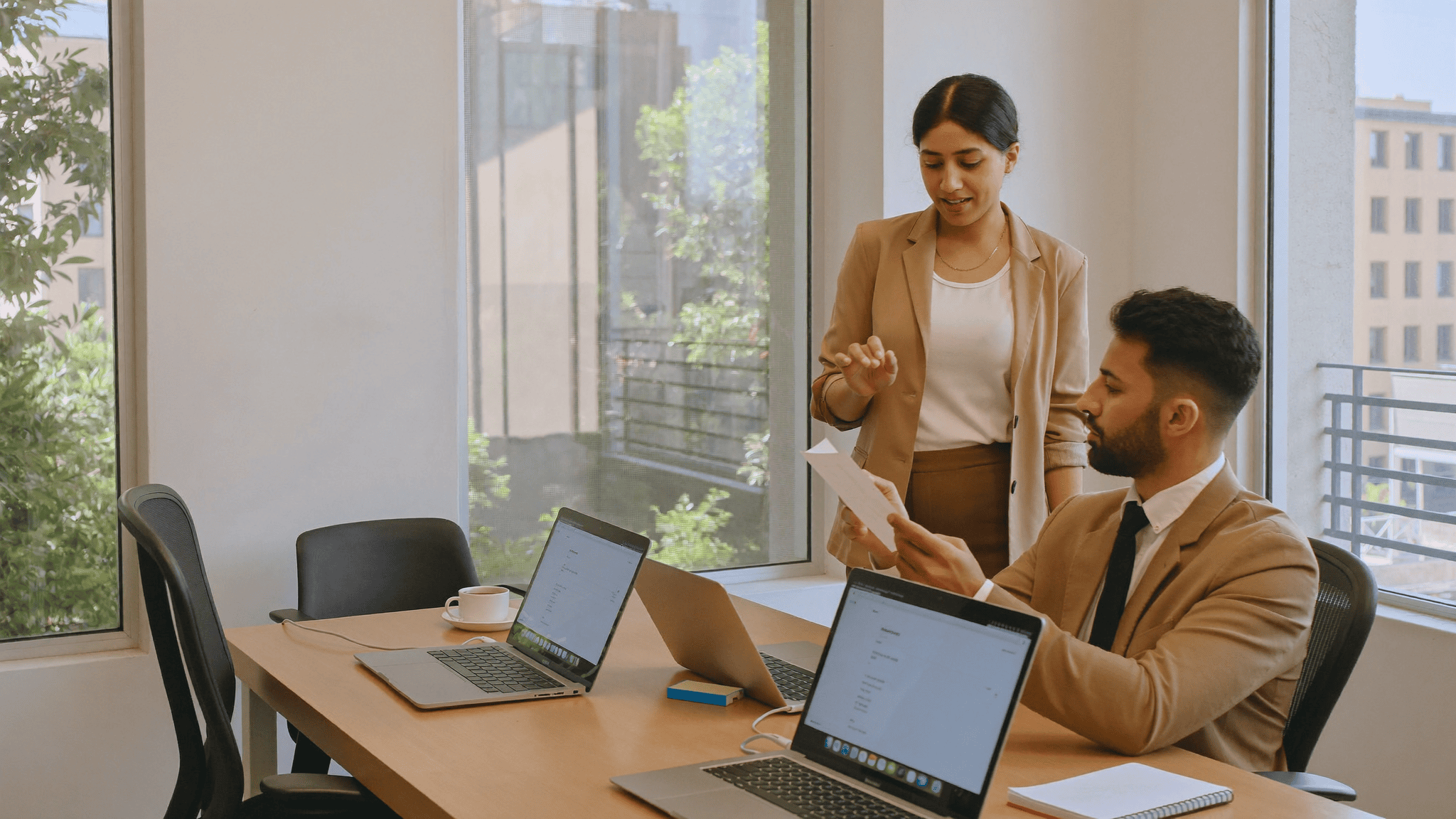 An IT manager and a finance colleague at a Navi Mumbai office desk reviewing a device contract beside a row of business laptops