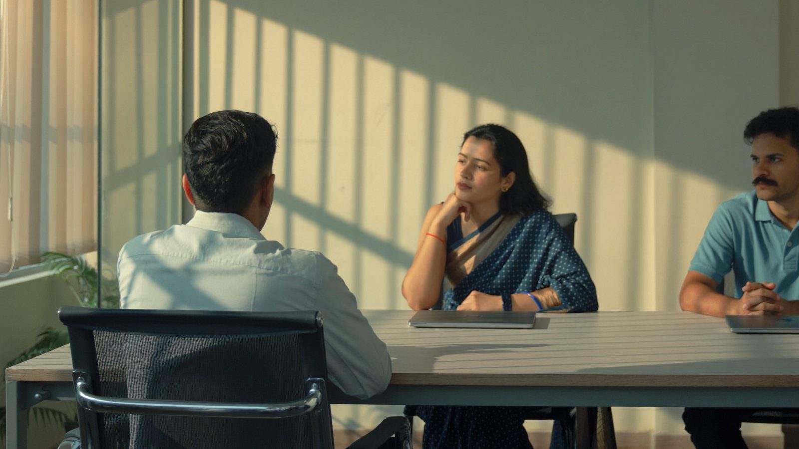 A finance head, an operations lead and an IT manager sitting around a plain table in an Indian office working out what their digital workplace costs per employee
