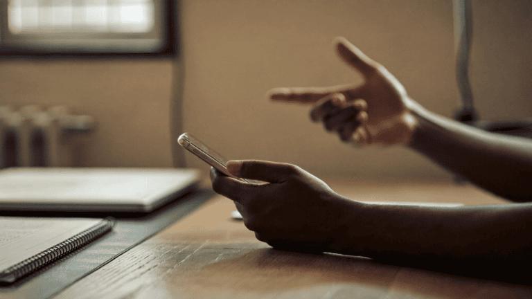 Hands of a salesperson holding a phone across a meeting room table in an Indian office, closed laptop beside them