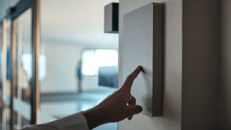 An office worker's finger reaching toward a plain wall-mounted access terminal at the glass-door entrance of a mid-size Navi Mumbai office