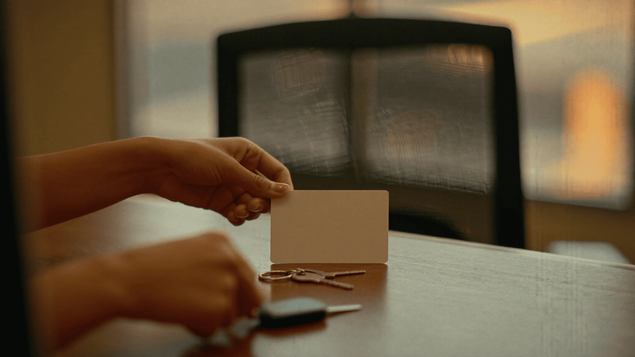 An employee’s hands leaving a blank access card and office keys on a desk beside an empty chair in warm evening light