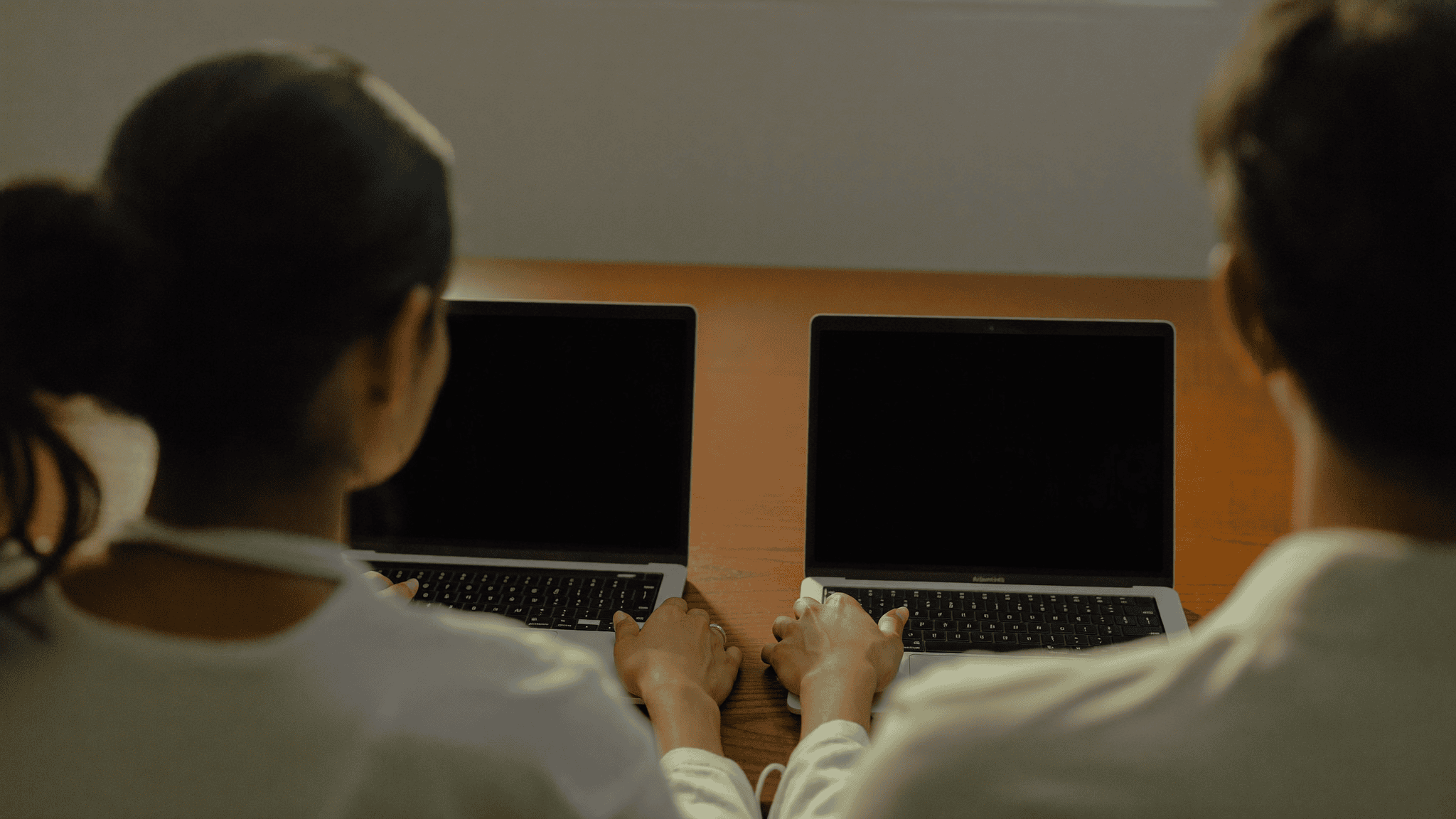 An IT security consultant and a business manager seen from behind, comparing two laptops with blank screens at a desk in a mid-size Navi Mumbai office
